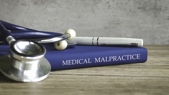 Stethoscope and a pen on a book titled MEDICAL MALPRACTICE, representing legal issues in healthcare.